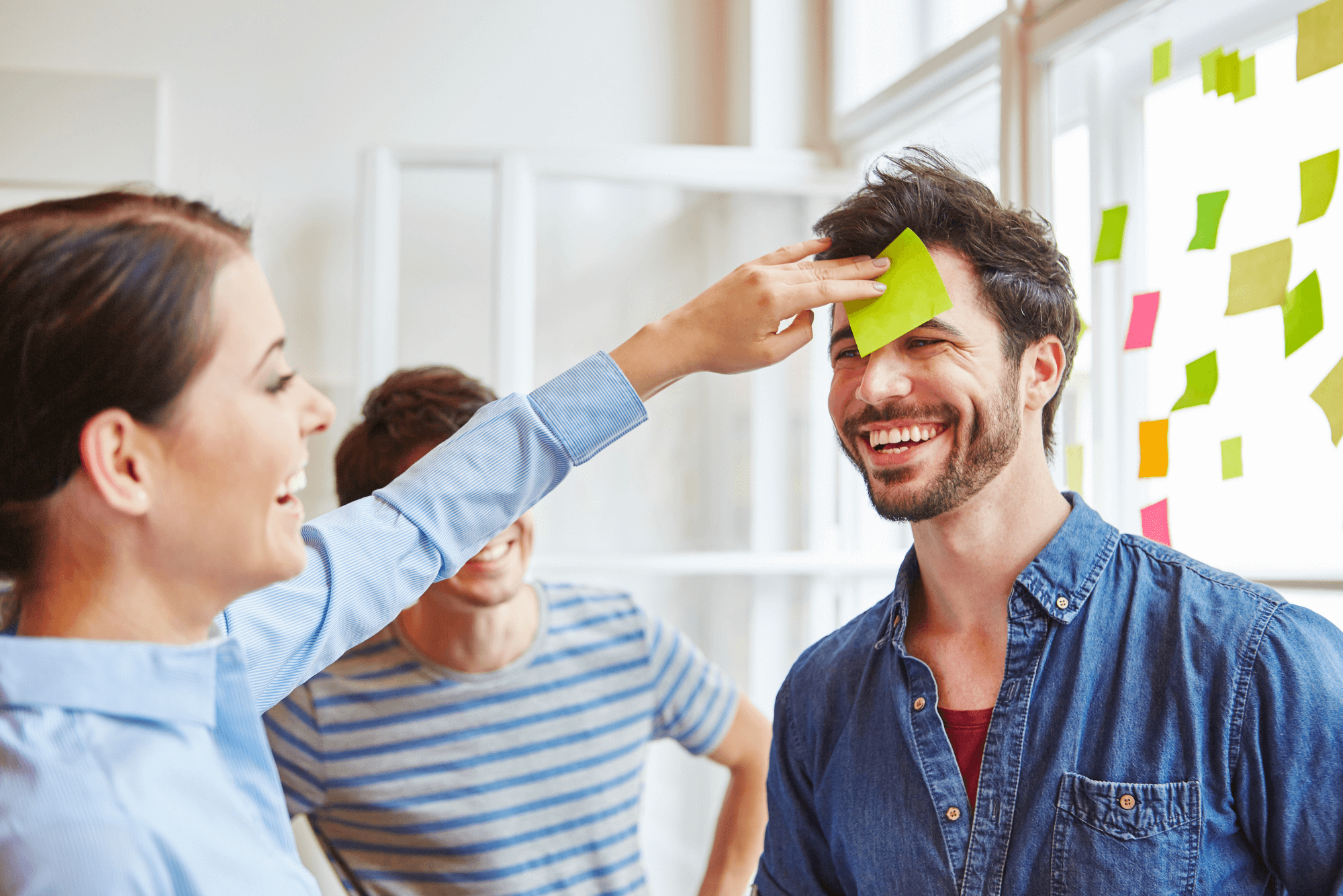 Mitarbeiter während eines Design Thinking Spiels, lachend und interagierend mit Post-it Notizen, umgeben von farbenfrohen Haftnotizen an den Fenstern. Text daneben beschreibt die Vision, Mission und Werte des Innovationscoachings von Patrick Falkenberg.